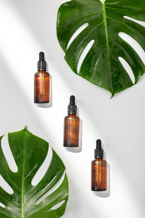 Herbal essential oils and tropical leaves on white background, flat lay, top view